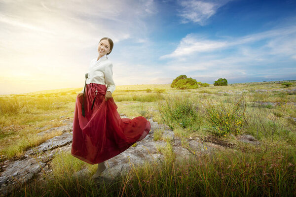 Asian woman wearing a traditional Korean national costume, Hanbok, standing on the meadow field with a blue sky background