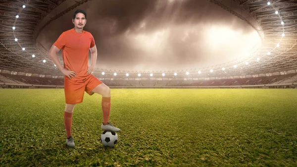 アジアのサッカー選手男でオレンジジャージの上にボールが立っていますサッカー場 — ストック写真