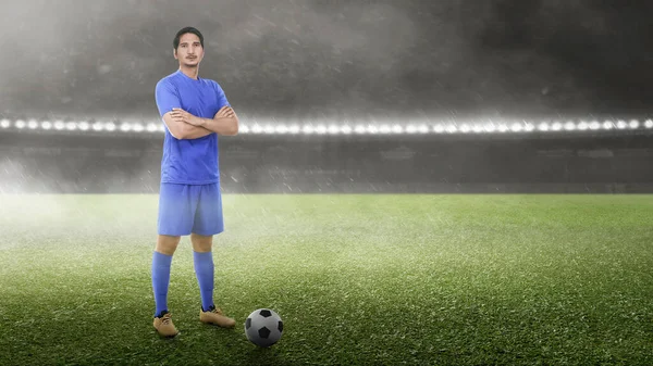 アジアのサッカー選手の男で青いジャージの上にボールが立っているサッカー場 — ストック写真