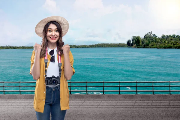 湖と青空を背景に興奮した表情の帽子とカメラを持つアジアの女性 — ストック写真