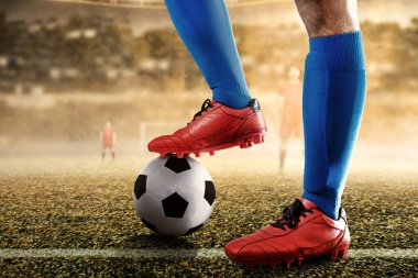 Futbol oyuncusu mavi formalı adam elinde topla futbol sahasında duruyor.