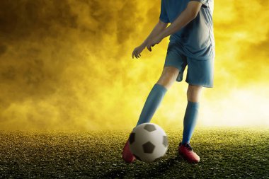 Mavi formalı bir futbolcu futbol sahasında topa vuruyor.