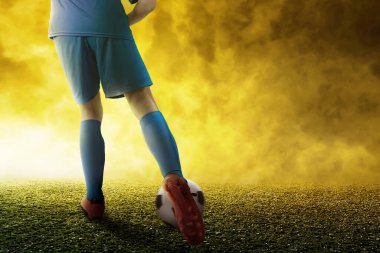 Mavi formalı bir futbolcunun futbol sahasında topa vuruşunun arka görüntüsü.
