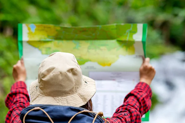 带着帽子和背包的亚洲女人在森林里拿地图的背景图 — 图库照片