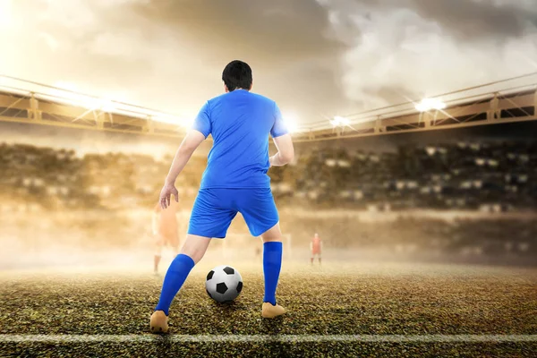 アジアのサッカー選手の背面図青いジャージの男がサッカー場でボールをドリブル — ストック写真