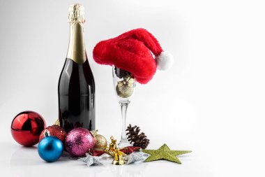 Noel Baba şapkalı şampanya şişesi ve beyaz arka planda Noel süslemeleri olan şampanya bardağı.