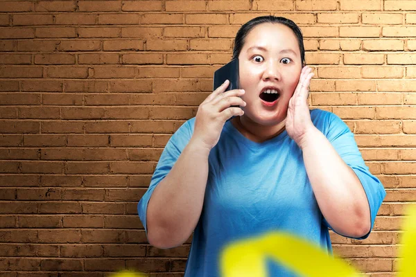 アジアの太った太りすぎの女性は携帯電話を保持し レンガの壁の背景と何かを叫んで — ストック写真