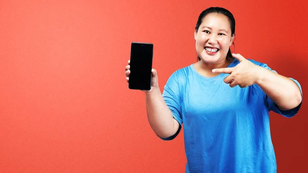 アジアの太った太りすぎの女性は 携帯電話を保持し 色の背景を持つ空の画面を示す — ストック写真