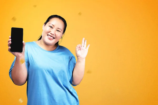 アジアの太った太りすぎの女性は 携帯電話を保持し 色の背景を持つ空の画面を示す — ストック写真