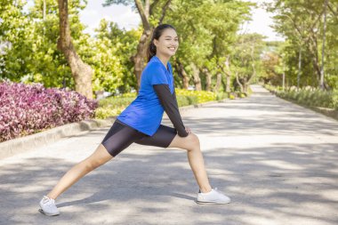 Asyalı kadın parkta koşmadan önce bacaklarını açıyor.