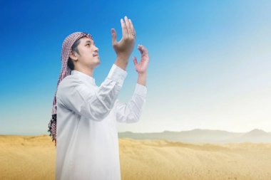 Keffiyeh ve agal ile Müslüman adam mavi gökyüzü arka planı ile el kaldırdı ve dua