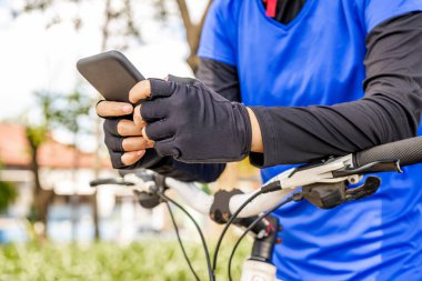 Parkta bisiklete binerken akıllı telefon kullanan bir kadın.