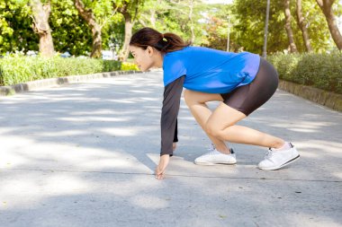Asyalı kadın başlangıç pozisyonunda parkta koşmaya hazır.