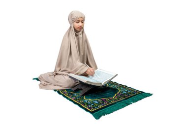 Asian Muslim girl in hijab on prayer rug reading the Quran isolated over white background