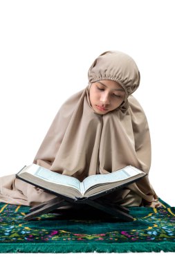 Asian Muslim girl in hijab on prayer rug reading the Quran isolated over white background