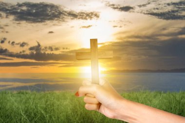 Human hand holding Christian cross with sunset sky background