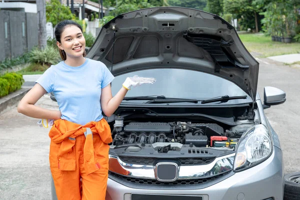 Asian women car technicians in uniform standing with open palms showing something in front of breakdown cars