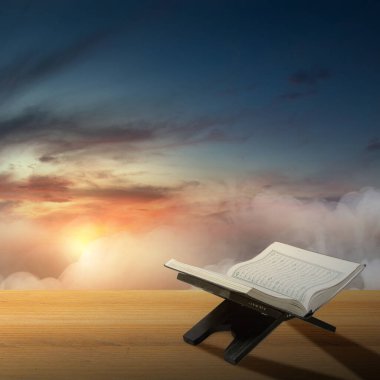 Opened Quran on a wooden placemat on the wooden board with a dramatic sky background
