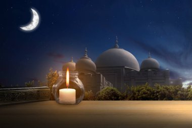 Gece sahnesinde camii olan ahşap masanın üzerine Kur 'an ve mum.
