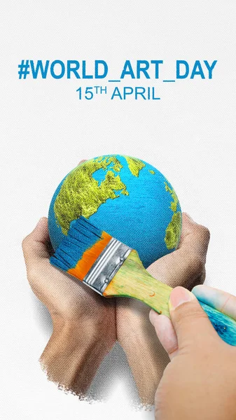A human hand with a paintbrush draws earth on a white canvas. World Art Day concept