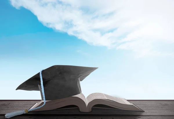 蓝天背景的翻开的书和毕业典礼帽 — 图库照片