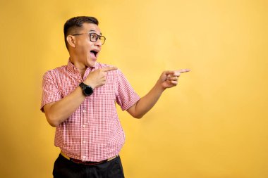 Gözlüklü ve gömlekli bir adam renkli arka plandaki bir şeyi işaret ediyor.