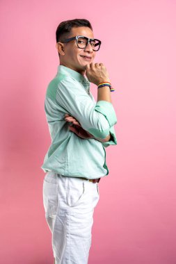 Gözlüklü ve gömlekli bir adam renkli bir arka planda gökkuşağı bileziği gösteriyor.