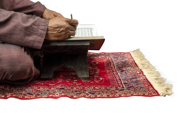 イスラム教徒の男が座って 白い背景に隔離された祈りの敷物の上にクルアーンを読んで — ストック写真