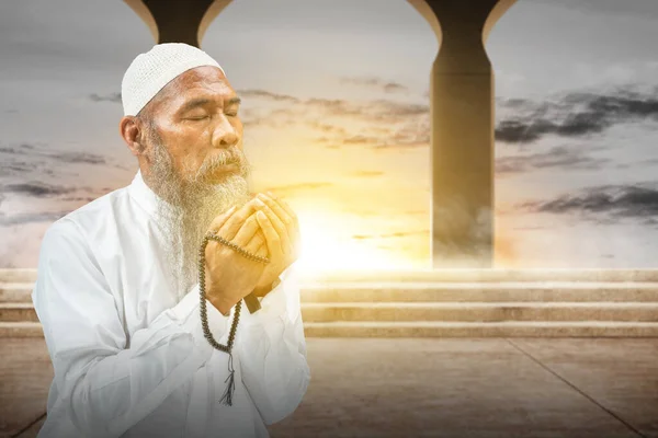 白い帽子をかぶっている髭を生やしたイスラム教徒の男は 日没シーンの背景と彼の手に祈りのビーズで祈っています — ストック写真