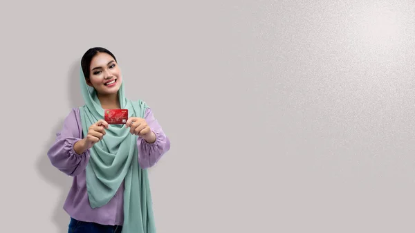 头戴头巾 持有彩色背景信用卡的亚洲穆斯林妇女 — 图库照片