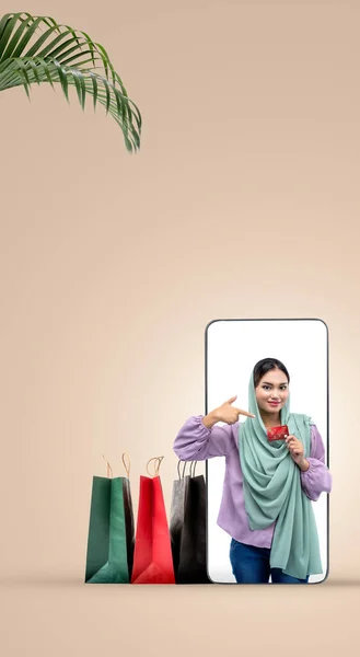 头戴头巾 手持信用卡 背景为彩色手机的亚洲穆斯林妇女 — 图库照片