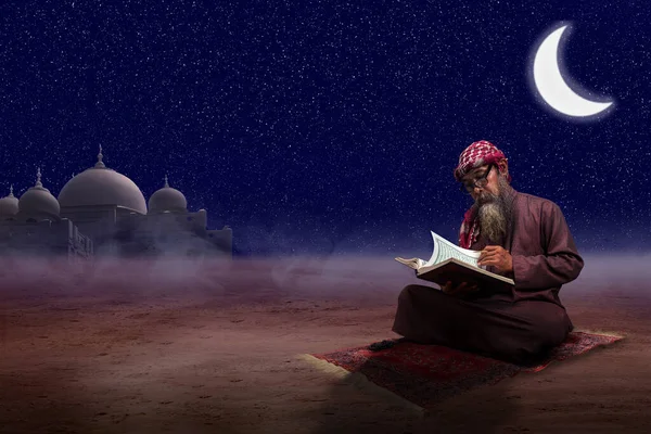 髭を生やしたイスラム教徒の男がKefiyehを着てアガル座って 夜のシーンの背景を持つ祈りの敷物の上でクルアーンを読んでいます — ストック写真