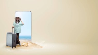 Plaj geçmişi olan bir cep telefonu ekranının önünde duran şapkalı ve valizli Asyalı kadın.