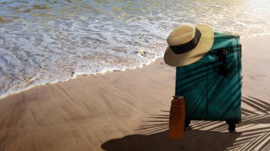 Okyanus dalgalarıyla dolu kumlu sahilde şapka ve bavul. Yaz konsepti