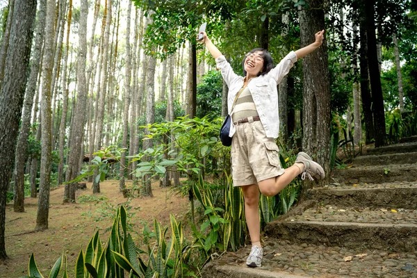 Azjatka Trzymająca Telefon Komórkowy Szczęśliwym Wyrazem Twarzy Lesie Działalność Podróżnicza — Zdjęcie stockowe