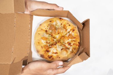 Beyaz arka planı olan karton bir kutuda pizza tutan bir insan eli.