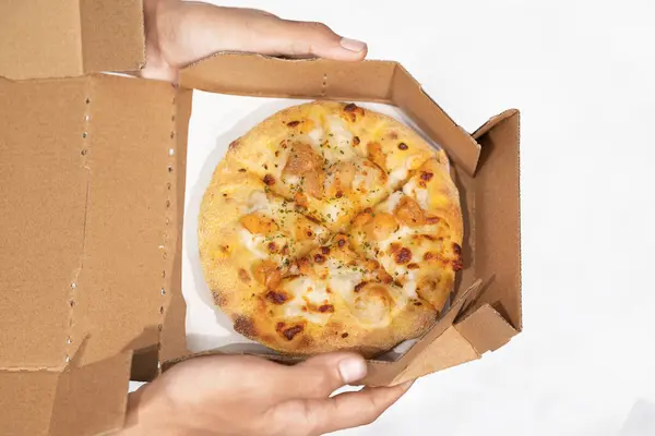 Beyaz arka planı olan karton bir kutuda pizza tutan bir insan eli.