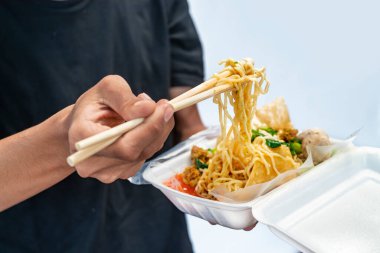 Beyaz arka planı olan tavuklu erişte (mie ayam) tutan bir insan eli. Geleneksel Endonezya yemekleri