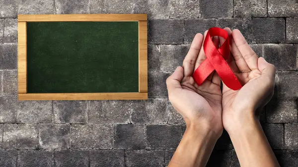 stock image Human hand showing red ribbon awareness with empty chalkboard. Empty chalkboard for copy space. World Aids Day concept