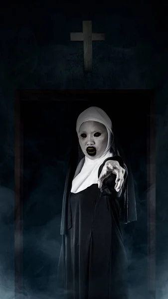 暗い背景に十字架とドアで立っている怖い悪魔修道女 怖い女性 ハロウィーンコンセプト — ストック写真