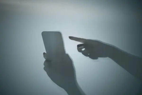 Shadow of a human hand holding a mobile phone on a colored background