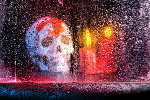 A human skull head and a candle with water drop in the window in a dark background. Scary skull Halloween concept