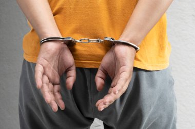 Elinde kelepçe, arka planında gri bir duvar olan tutuklu bir adam.