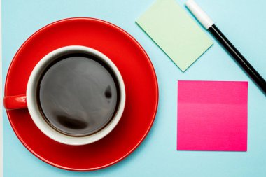 Renkli arka planda işaretli bir fincan kahve ve not kağıdı.