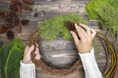 Ahşap masa arkasında insan eli Noel çelengi yapıyor. Noel dekorasyonu konsepti