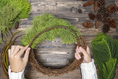 Ahşap masa arkasında insan eli Noel çelengi yapıyor. Noel dekorasyonu konsepti