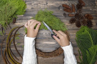 Ahşap masa arkasında insan eli Noel çelengi yapıyor. Noel dekorasyonu konsepti