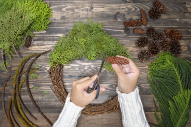 Ahşap masa arkasında insan eli Noel çelengi yapıyor. Noel dekorasyonu konsepti