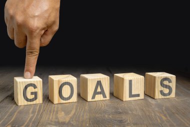 Bir insan eli ahşap bir masanın üzerinde GoALS harfleri olan tahta küpleri gösterir. Başarı için planlama kavramı