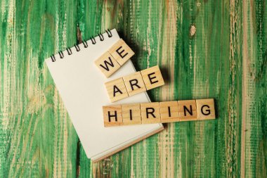 Wooden cubes with We Are Hiring letters and an empty notebook on a wooden background. Empty notebook for copy space. Human resources management concept
